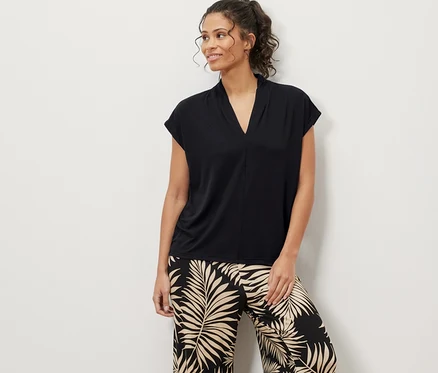 Une femme debout portant une blouse noire avec encolure en V et un pantalon à motif de feuilles.