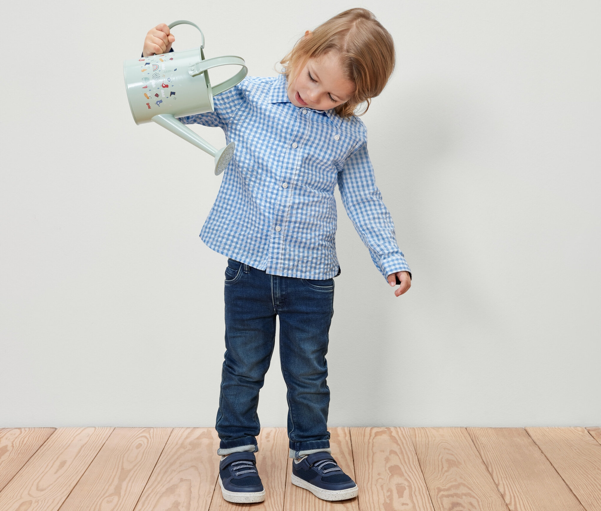 Un garçon tient un arrosoir bleu clair. Il porte une chemise pour enfant.