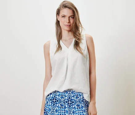 Femme portant un chemisier sans manches en lin, blanc, et une jupe bleue.