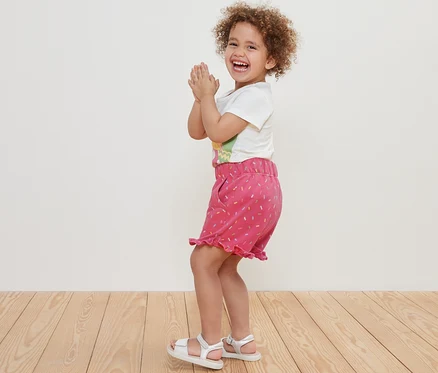 Fillette souriante aux cheveux bouclés applaudissant en sweat-short pour enfants.