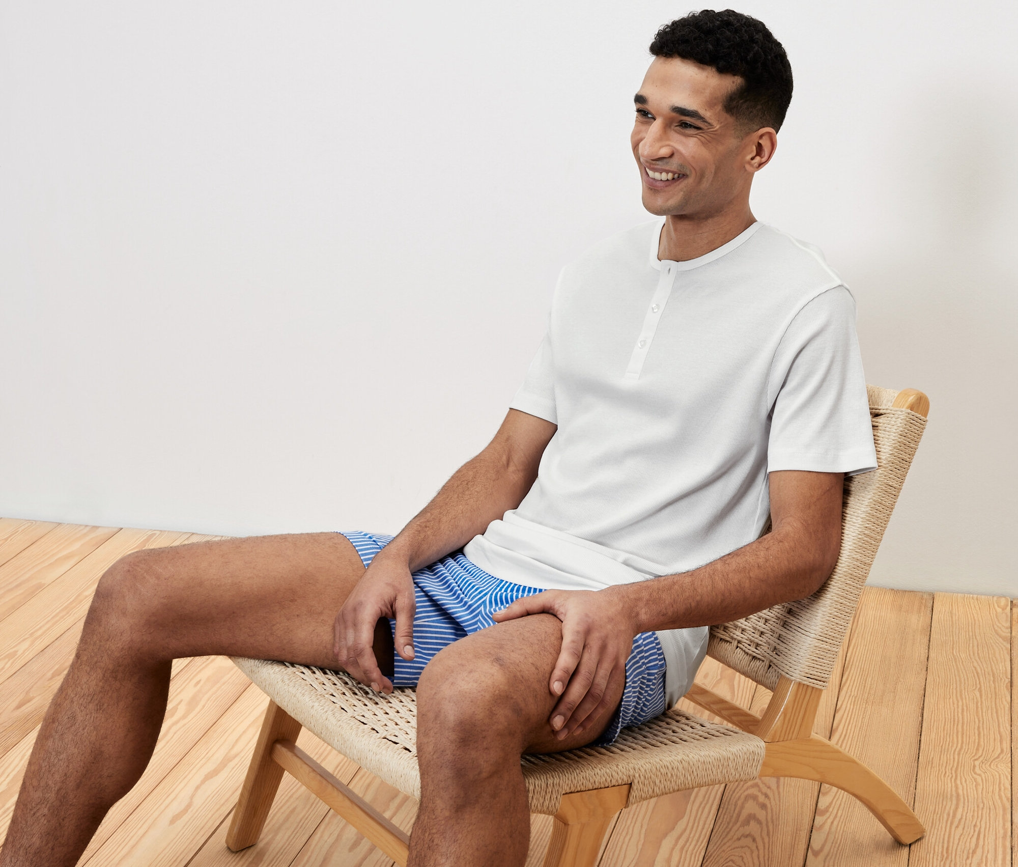 Un homme est assis sur une chaise en ensemble pyjama shorty et sourit.