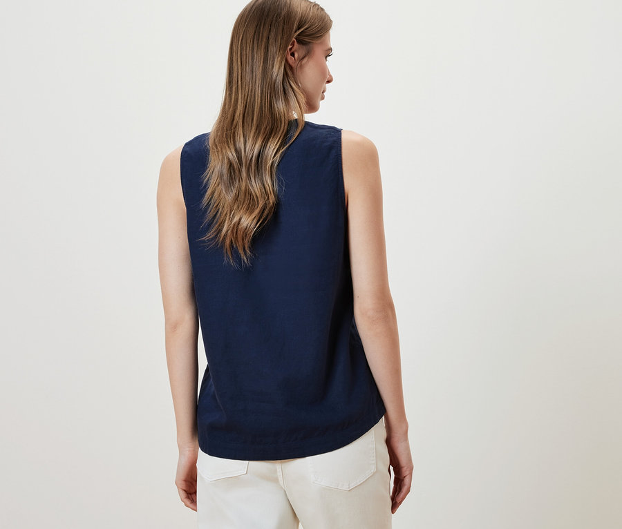 Une femme porte un chemisier sans manches en lin bleu marine et un pantalon blanc.