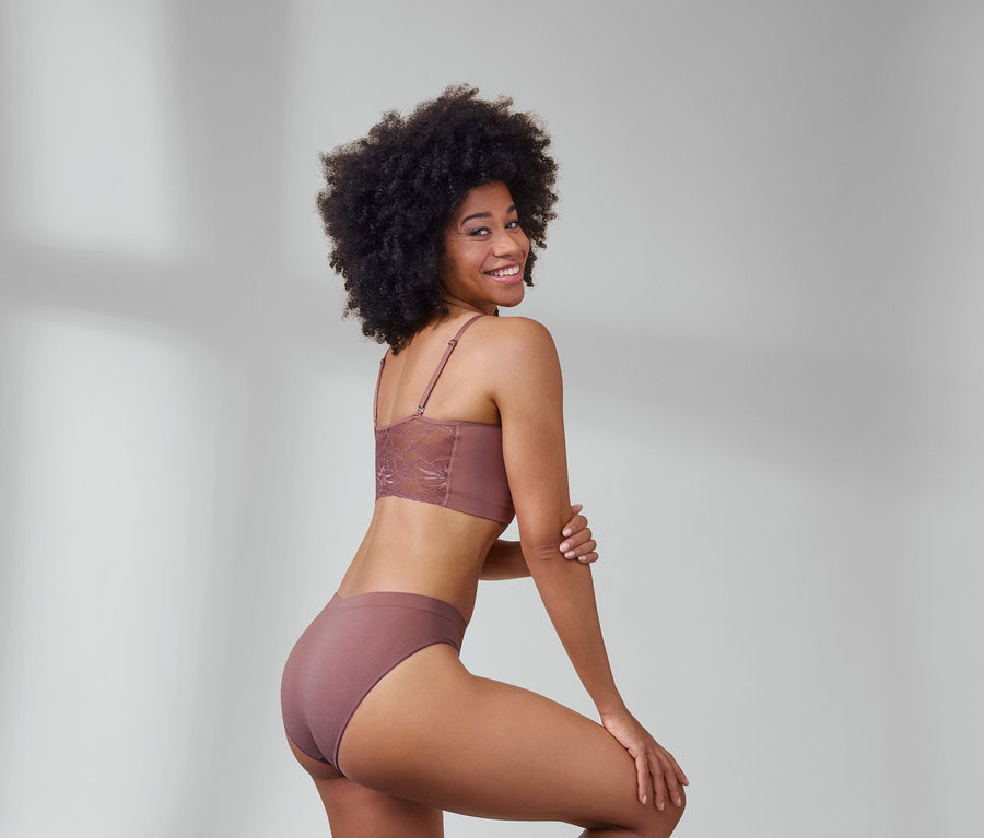 Une femme pose en brassière seamless avec dentelle marron et 2 slips seamless marron.
