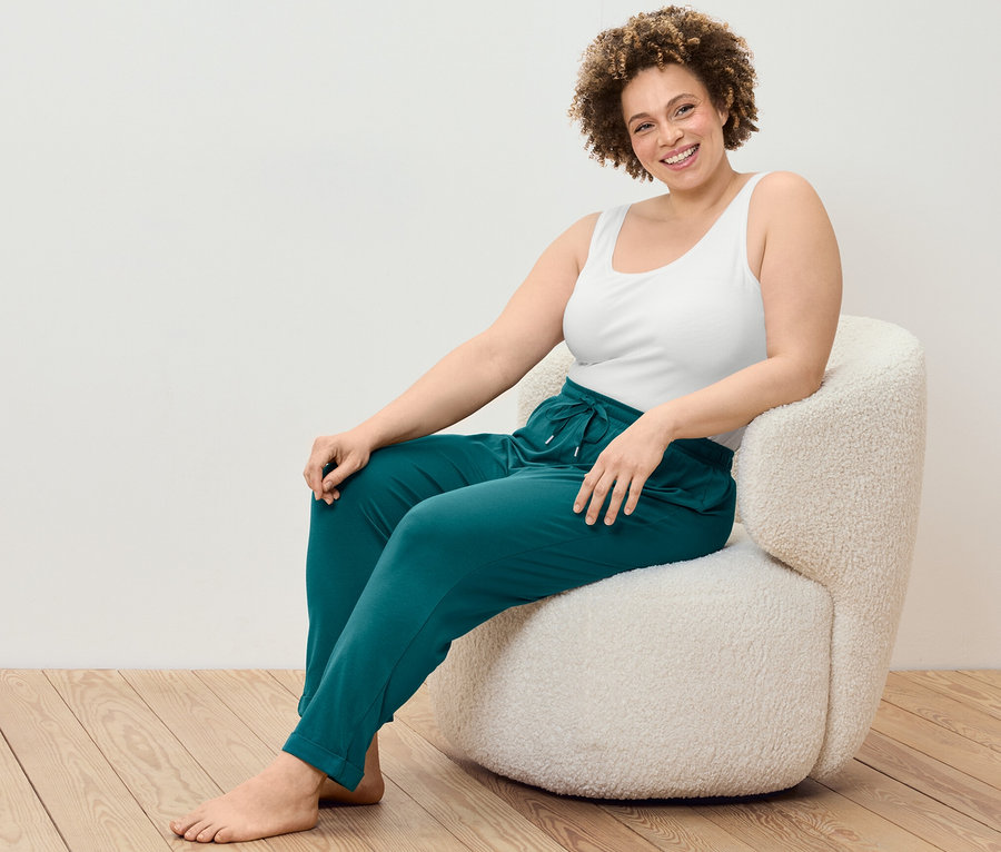 Une femme est assise dans un fauteuil et porte un 2
débardeurs et un pantalon de pyjama.