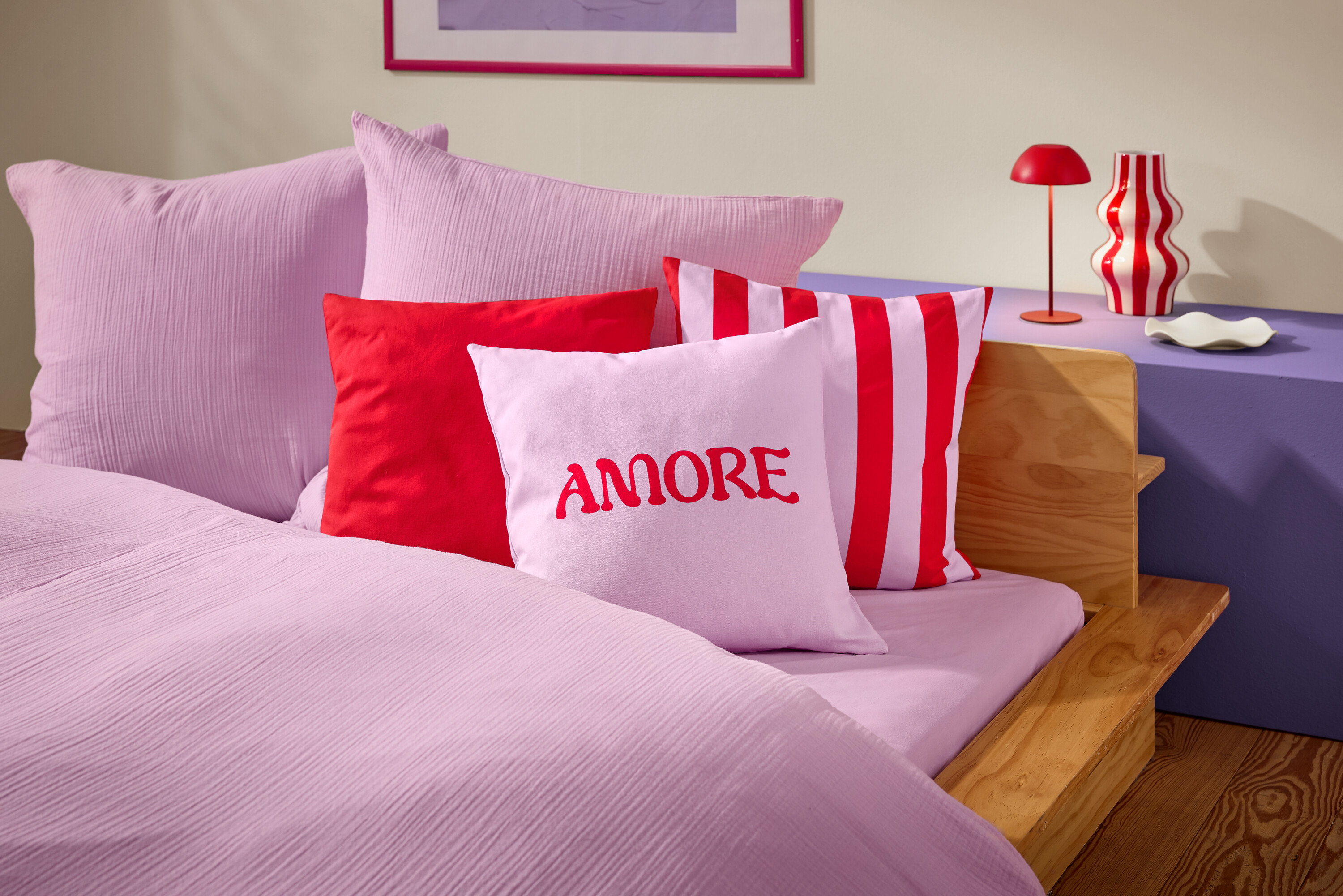 Gros plan d'un lit avec des draps et des oreillers roses. Un oreiller porte le mot AMORE en rouge.