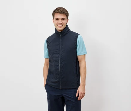 Un homme souriant regarde la caméra et porte un gilet bleu marine sur un t-shirt bleu clair.