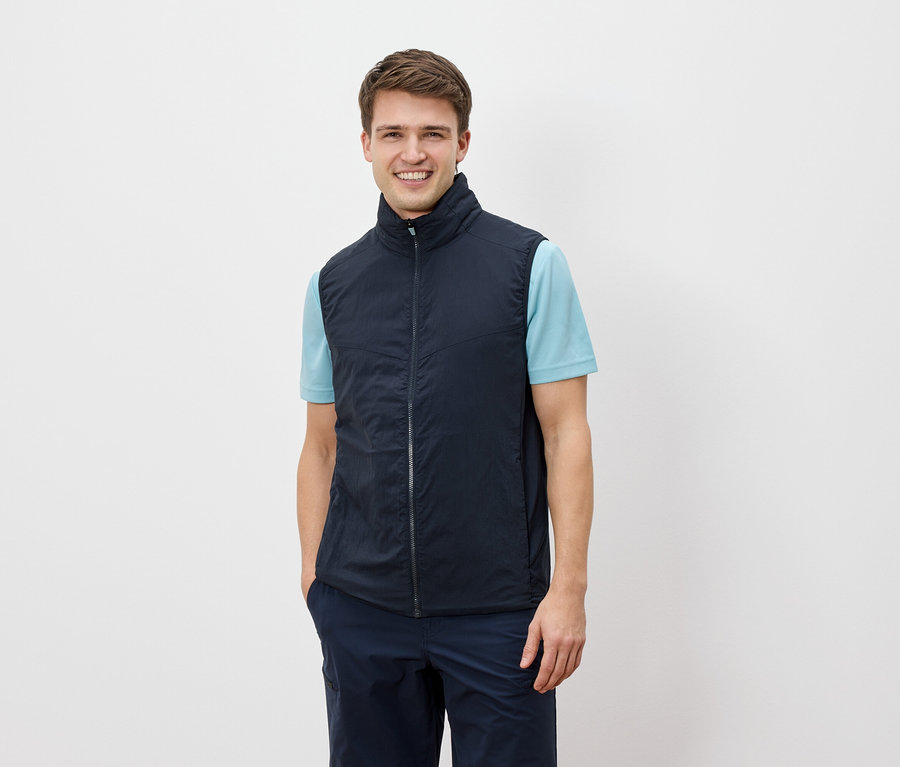 Un homme souriant regarde la caméra et porte un gilet bleu marine sur un t-shirt bleu clair.