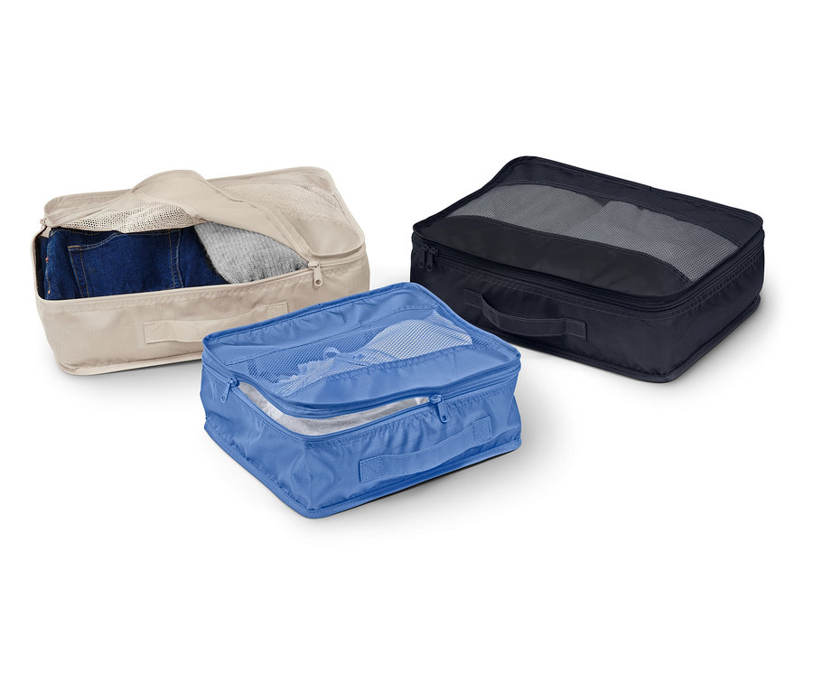 Trois boîtes de rangement en tissu beige, bleue et noire sont posées sur un fond blanc.