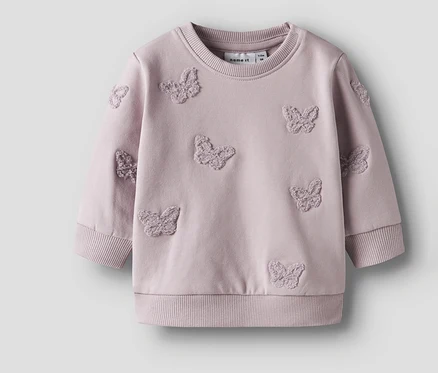 Un sweat-shirt pour bébé NAME IT lilas avec des papillons cousus est posé sur un fond neutre.