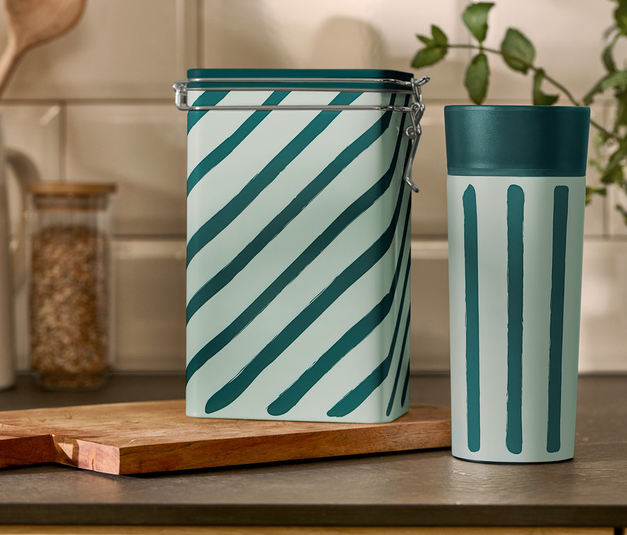 Une boîte à café rayée et un gobelet de voyage sont posés sur une table de cuisine.