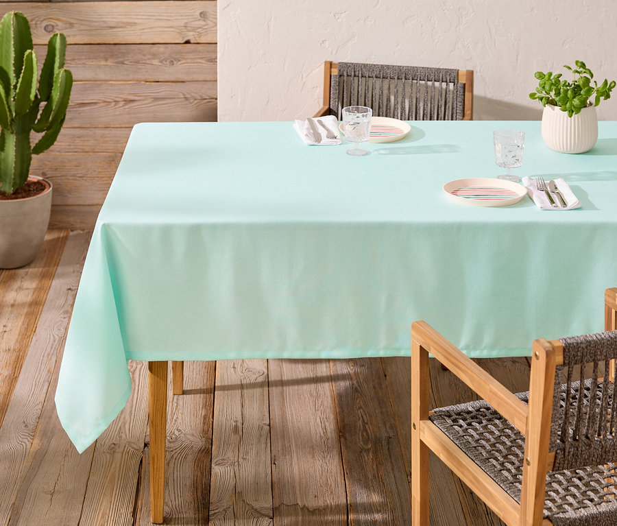 Table à manger avec nappe turquoise clair, couverts et cactus en pot.