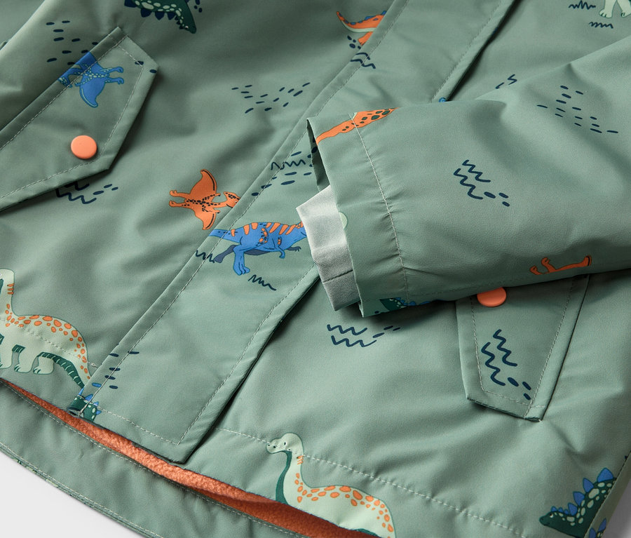Gros plan sur une veste vert clair à motifs de dinosaures, fermeture boutonnée et poches.