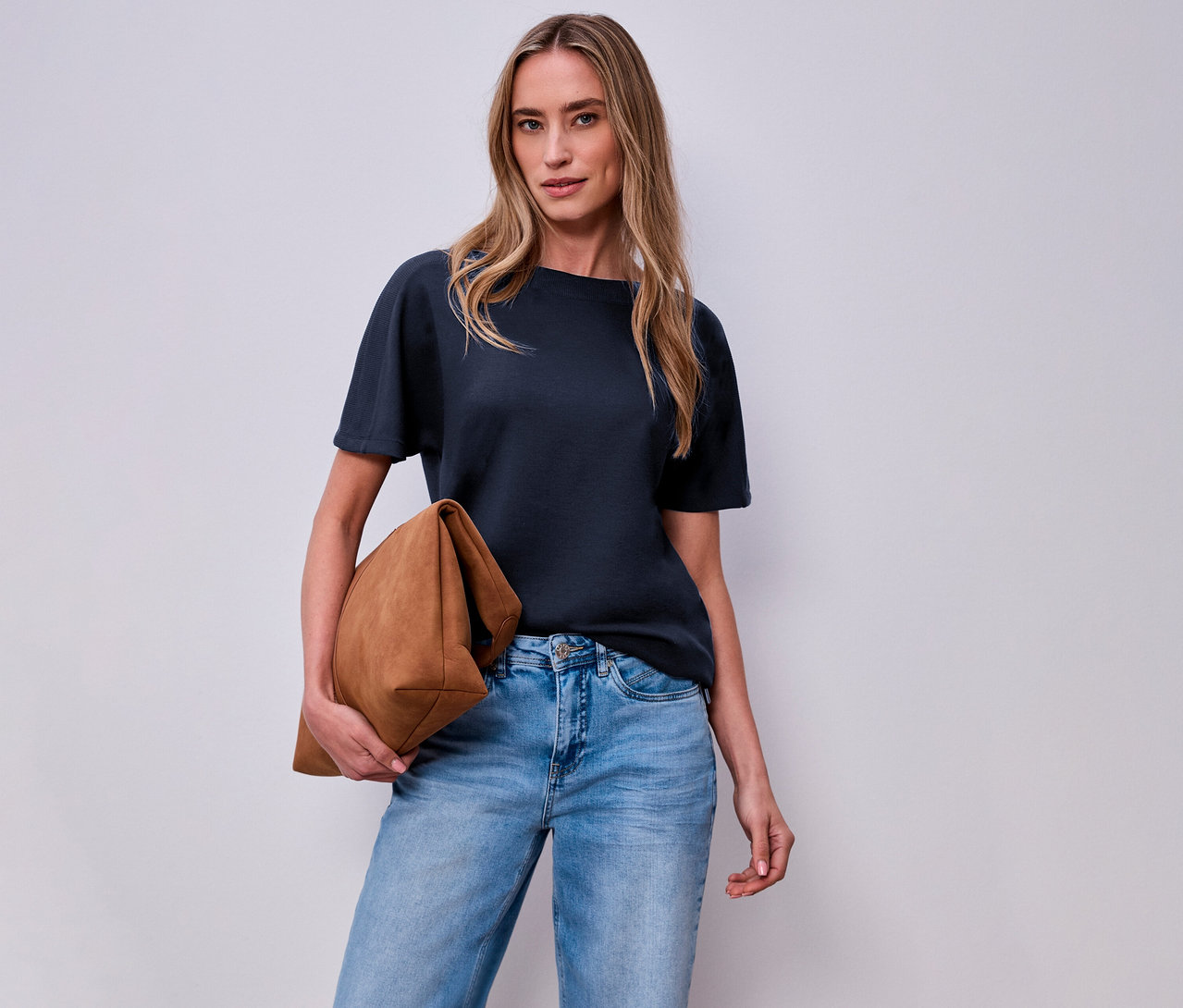 Femme avec un sac marron et une chemise à manches courtes Street One bleu marine devant un mur blanc.