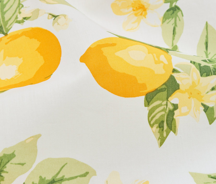 Gros plan d'un tissu à motifs de citrons et de fleurs dans des tons jaunes et verts sur fond blanc.