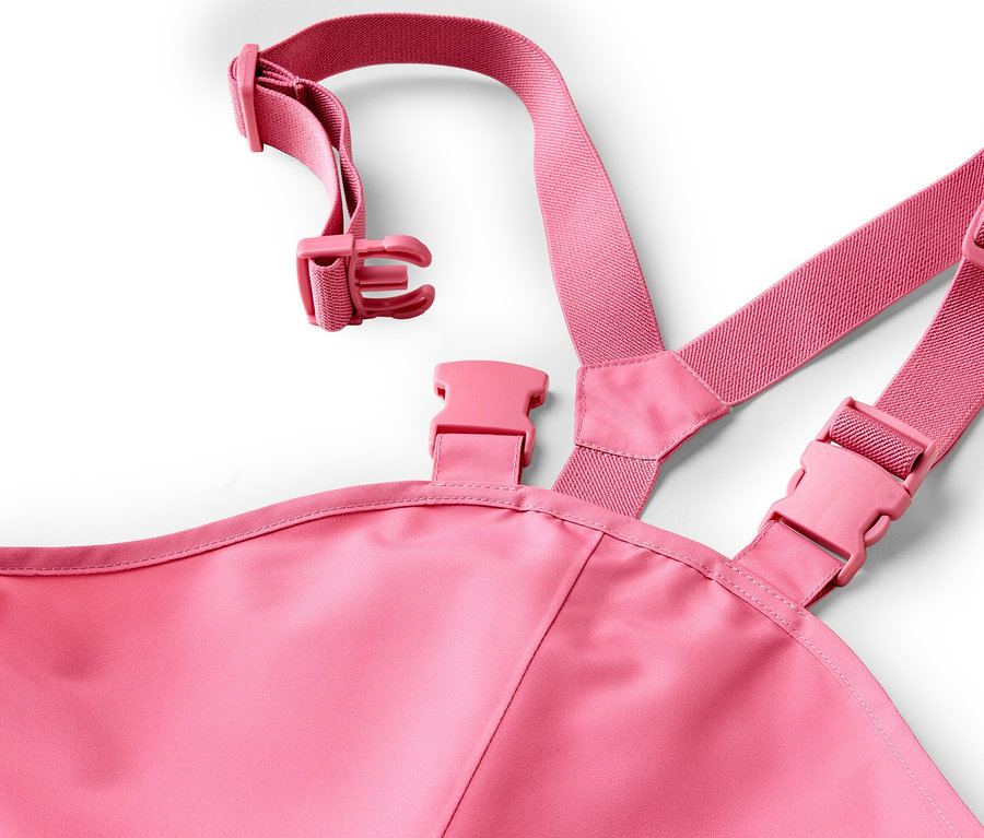 Gros plan d'une salopette rose avec des bretelles réglables et des boucles sur fond blanc.