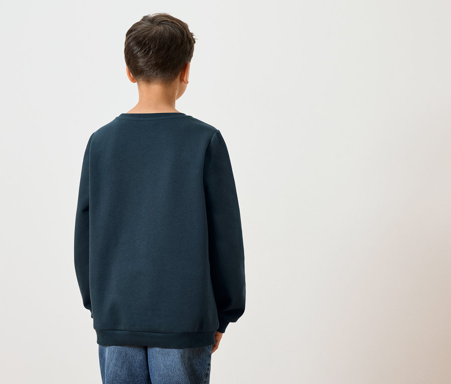 Vue arrière d'un enfant aux cheveux foncés portant un sweat-shirt bleu marine et un jean bleu sur fond blanc.