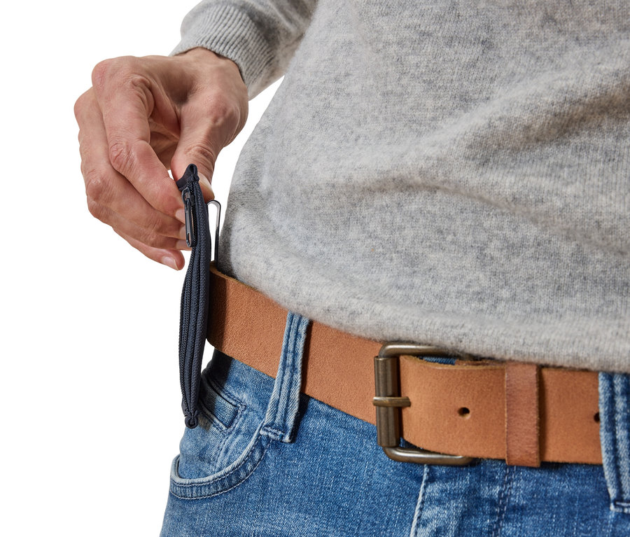 Gros plan d'une personne attachant une fine pochette zippée bleu marine à une ceinture en cuir marron, portée sur un jean bleu.