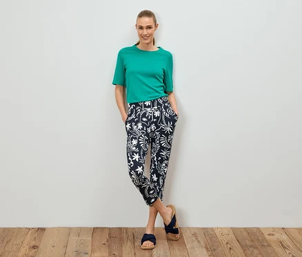 Une femme se tient debout, les mains dans les poches, portant un t-shirt vert et un pantalon à motifs.