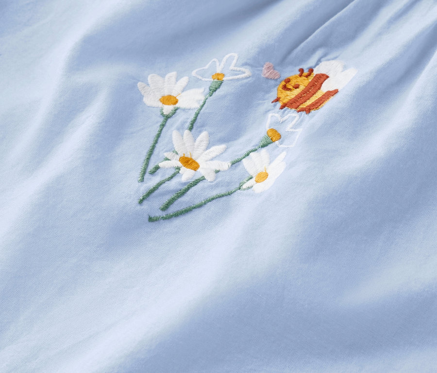 Gros plan d'un tissu bleu clair avec des marguerites brodées et une abeille.