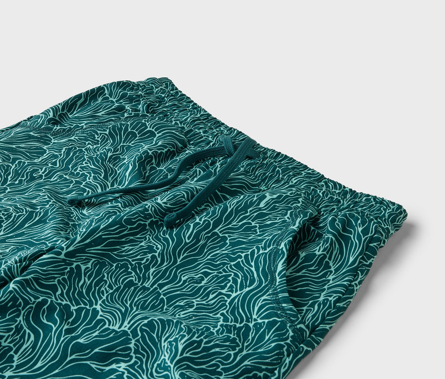 Gros plan d'un pantalon vert avec un motif de vagues blanches, un cordon de serrage et une poche latérale sur un fond blanc.