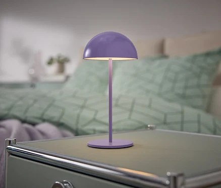 Une lampe violette est posée sur une table de chevet à côté d'un lit.