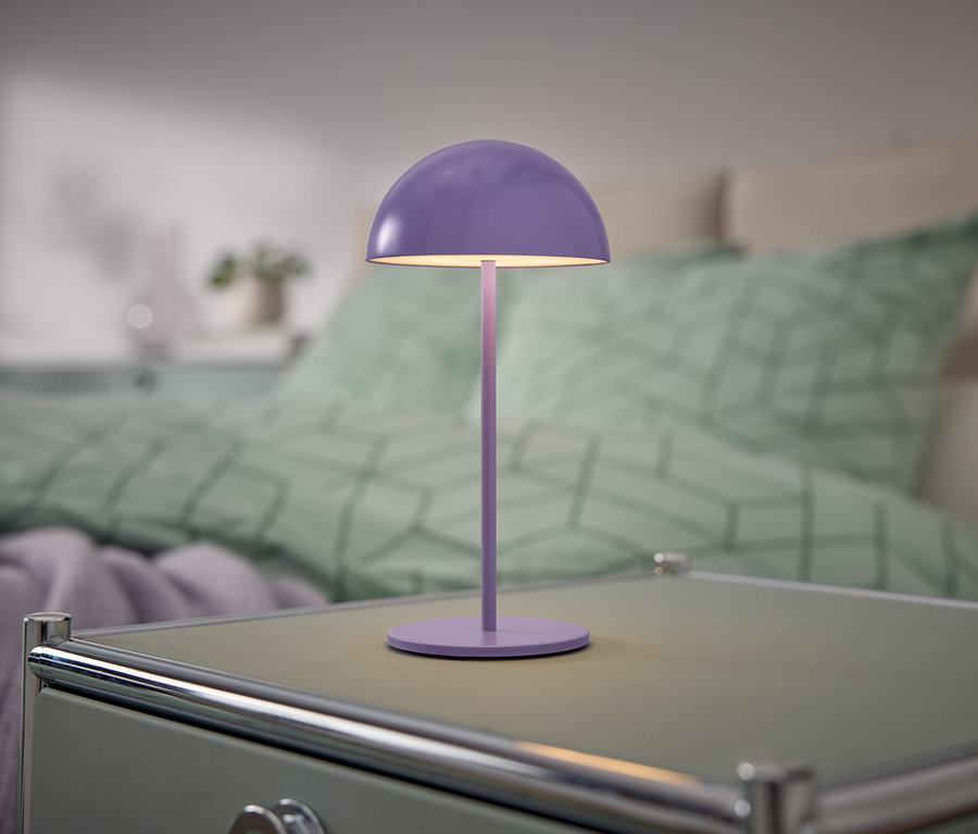 Une lampe violette est posée sur une table de chevet à côté d'un lit.