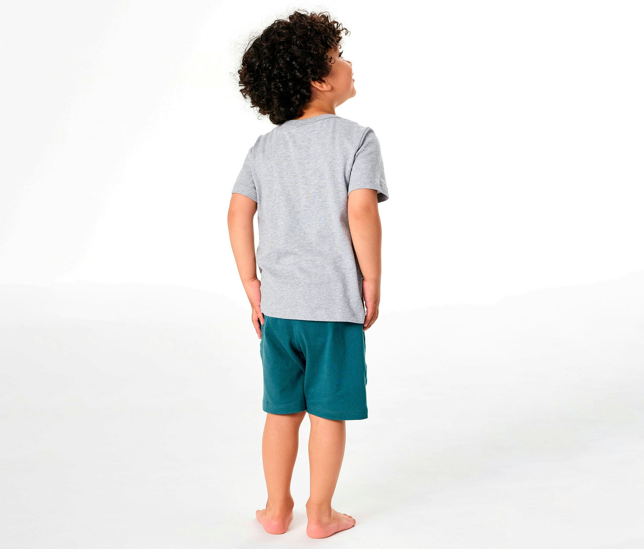 Garçon vu de dos portant un pyjama court pour enfant SCHIESSER composé d'un t-shirt gris et d'un short vert, regardant vers le haut.