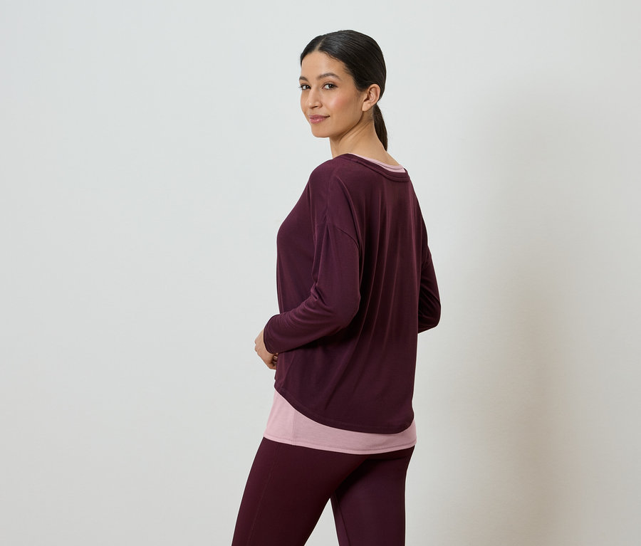 Femme portant un haut à manches longues bordeaux sur un haut rose et un legging bordeaux.