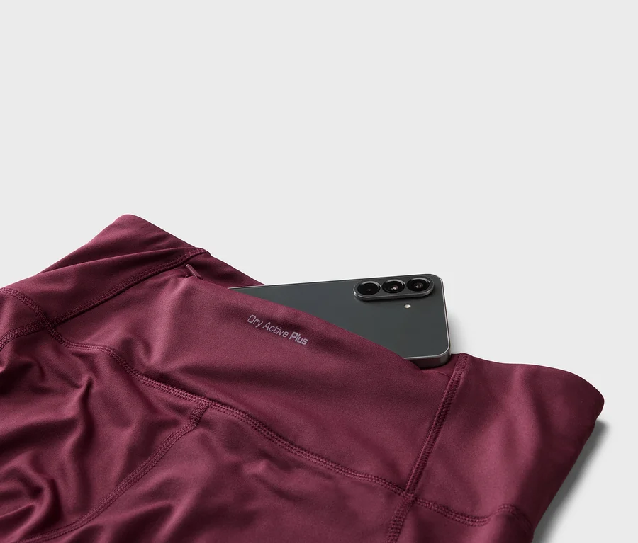 Gros plan d'un legging bordeaux avec l'inscription « Dry Active Plus » et un smartphone noir dans la poche.