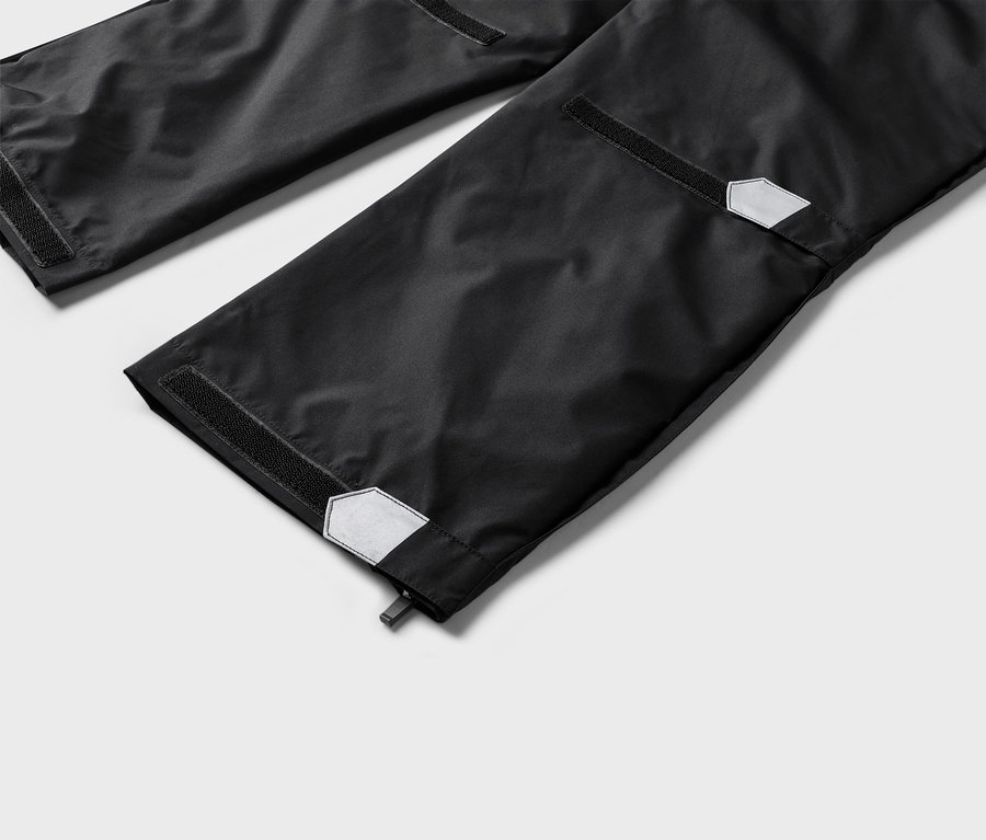 Gros plan sur le bas de jambes d'un pantalon noir avec des fermetures velcro et des détails réfléchissants aux extrémités.