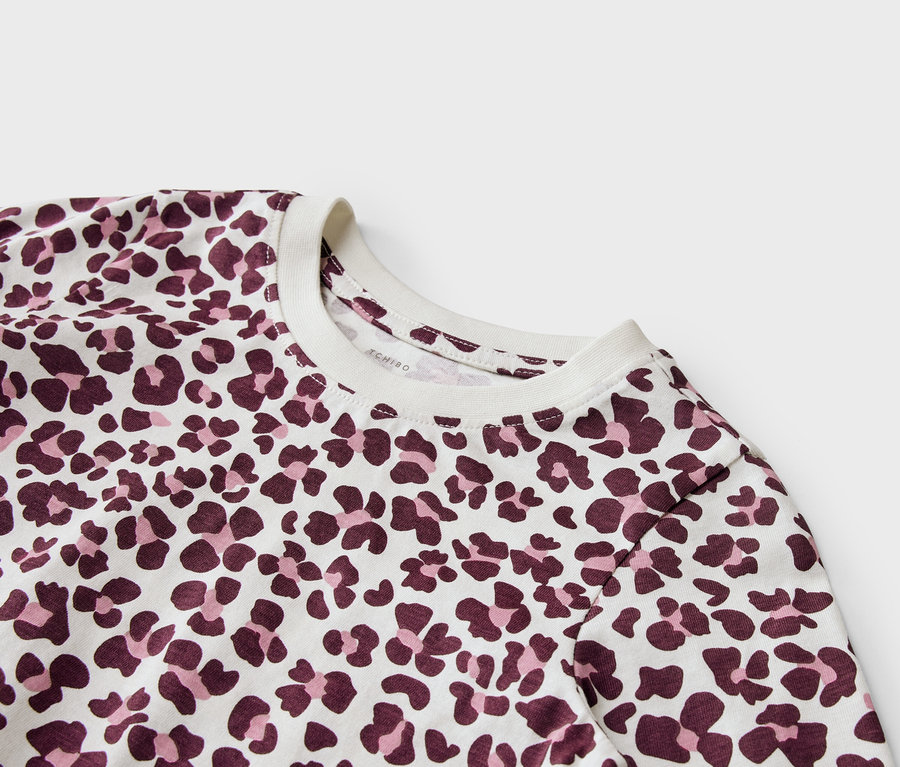 Gros plan d'un haut blanc à manches longues avec un motif floral rouge foncé et rose clair.