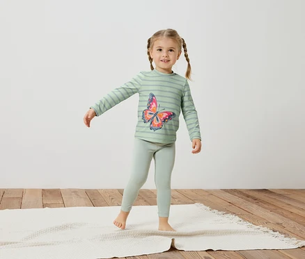Fillette avec des tresses, portant un haut rayé vert clair avec un imprimé papillon et un legging.