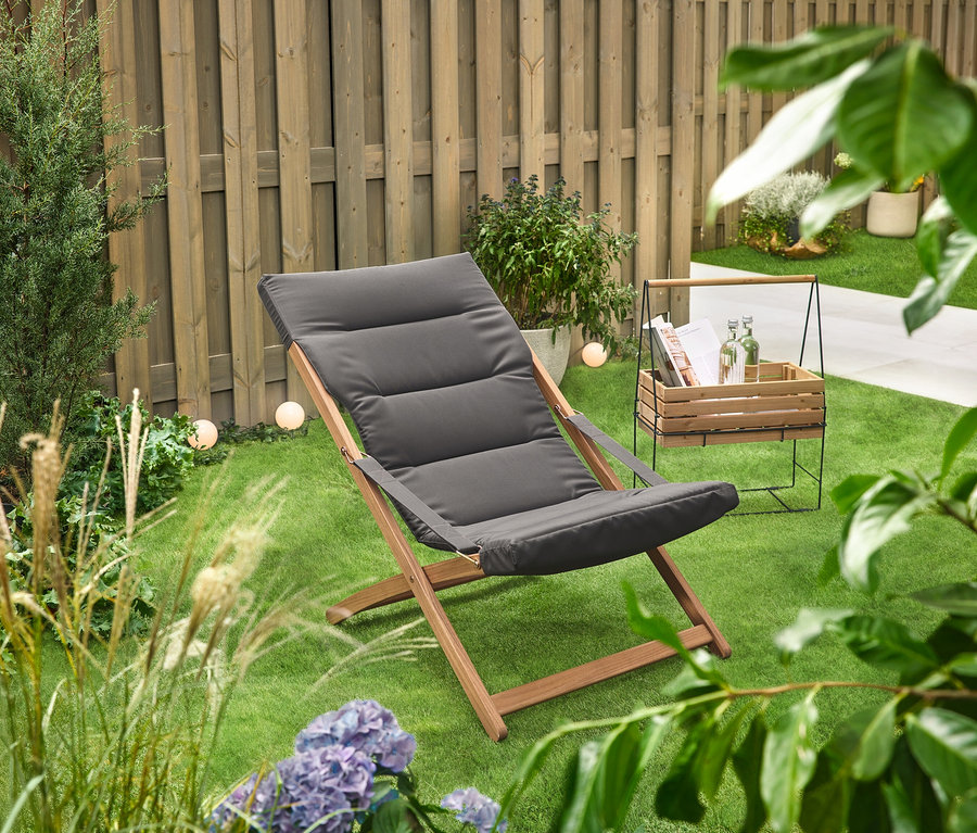 Sur une pelouse verte se trouve un bac à herbes aromatiques avec support de transport »Elin« à côté d'une chaise longue.