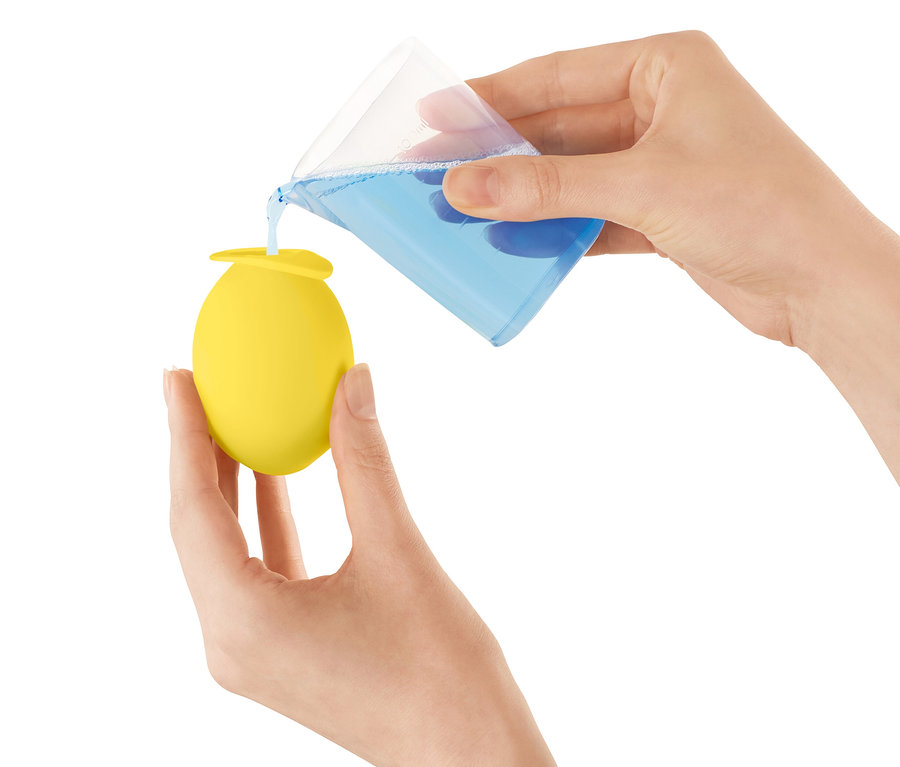 Une personne verse un liquide bleu d'un verre doseur dans un récipient jaune en forme d'œuf.
