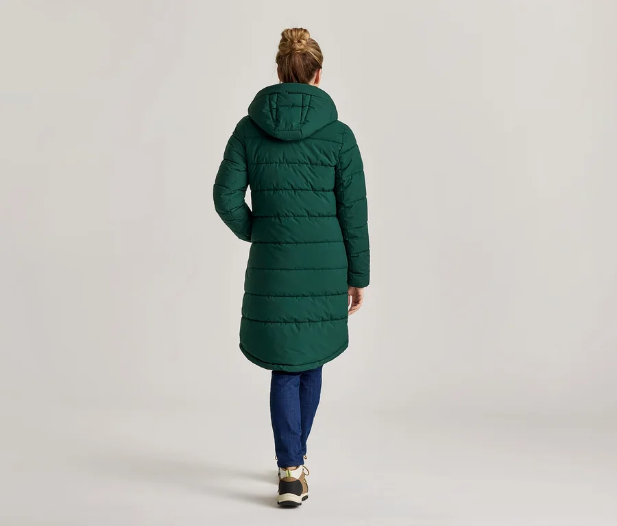 Vue arrière d'une femme portant un chignon, un long manteau matelassé vert à capuche, un jean et des baskets.
