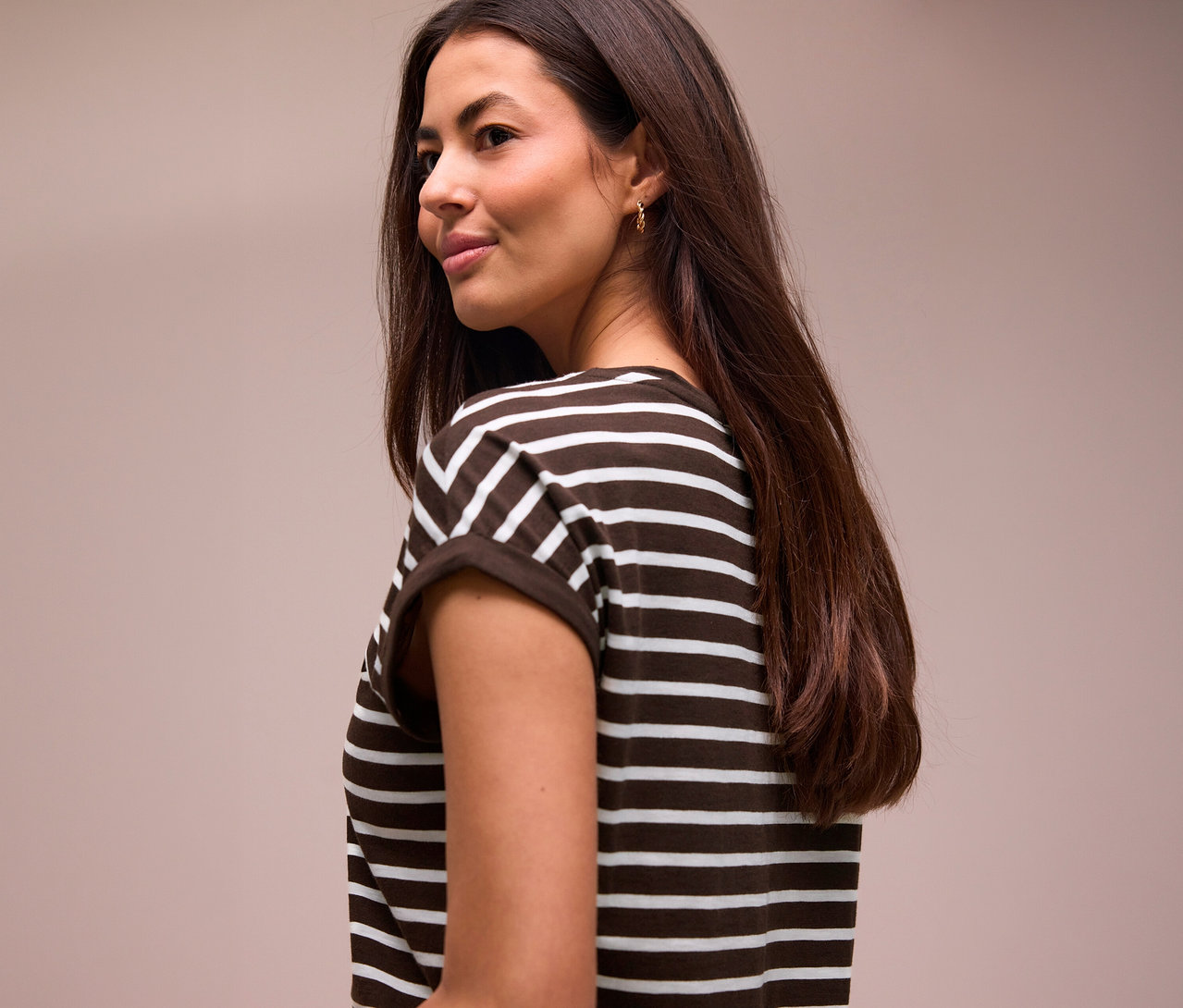 Femme aux longs cheveux foncés regardant par-dessus son épaule, portant un T-shirt Street One rayé marron et blanc.