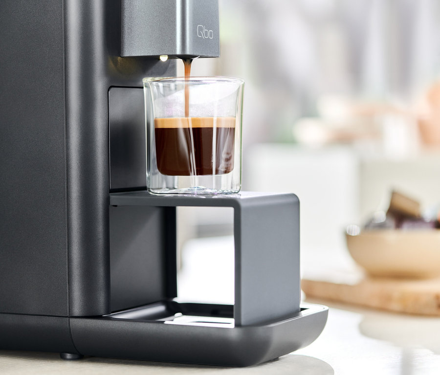 Le café est versé dans un verre à partir d'une machine à café Qbo ESSENTIAL Dark Stone.