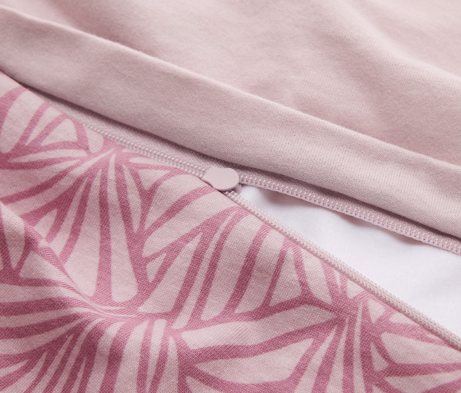 Gros plan d'un tissu en deux tons de rose. Une partie présente un motif géométrique rose foncé, l'autre partie est unie rose clair. Une fermeture éclair rose est partiellement ouverte, révélant une doublure blanche.