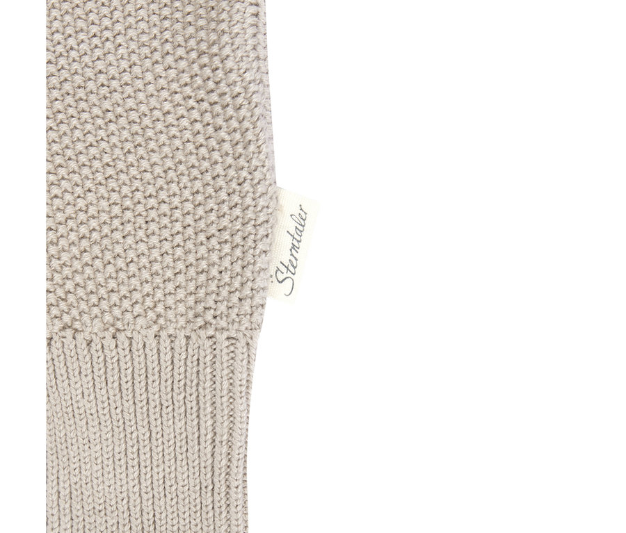 Gros plan d'un tissu tricoté beige avec une étiquette blanche "Sterntaler". Le tissu présente un bord côtelé et un motif tricoté texturé.