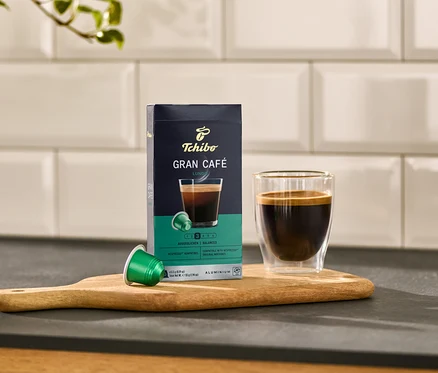 Sur une planche en bois, une boîte de Gran Café Lungo, une capsule verte et un verre de café.