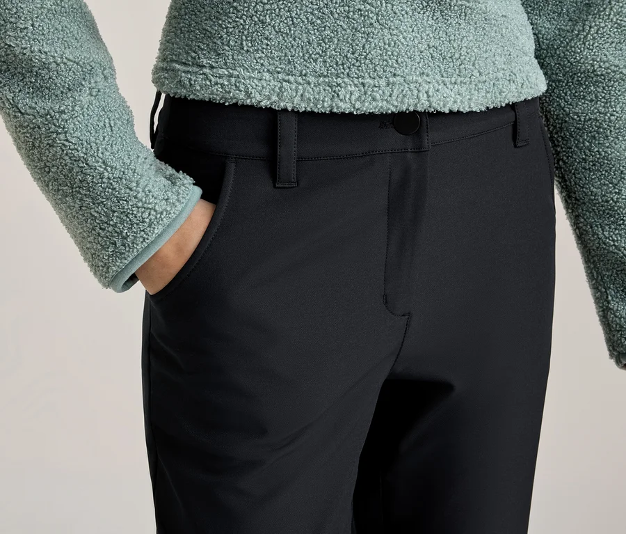 Personne vêtue d'un haut vert clair duveteux et d'un pantalon noir, une main dans la poche.