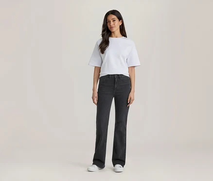 Femme debout, portant un t-shirt blanc, un jean gris foncé et des baskets blanches.
