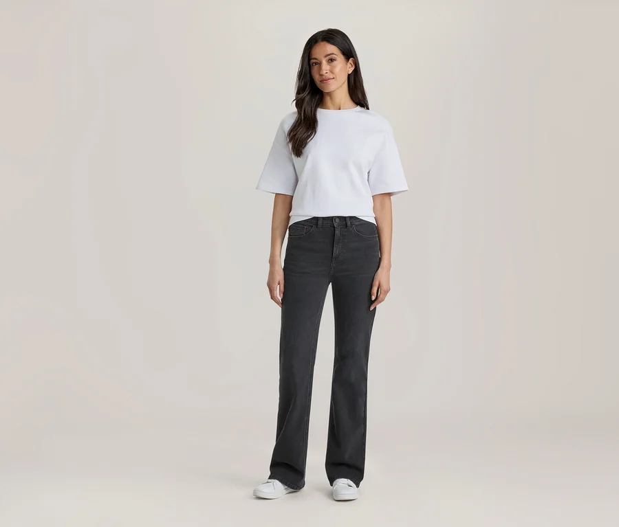 Femme debout, portant un t-shirt blanc, un jean gris foncé et des baskets blanches.