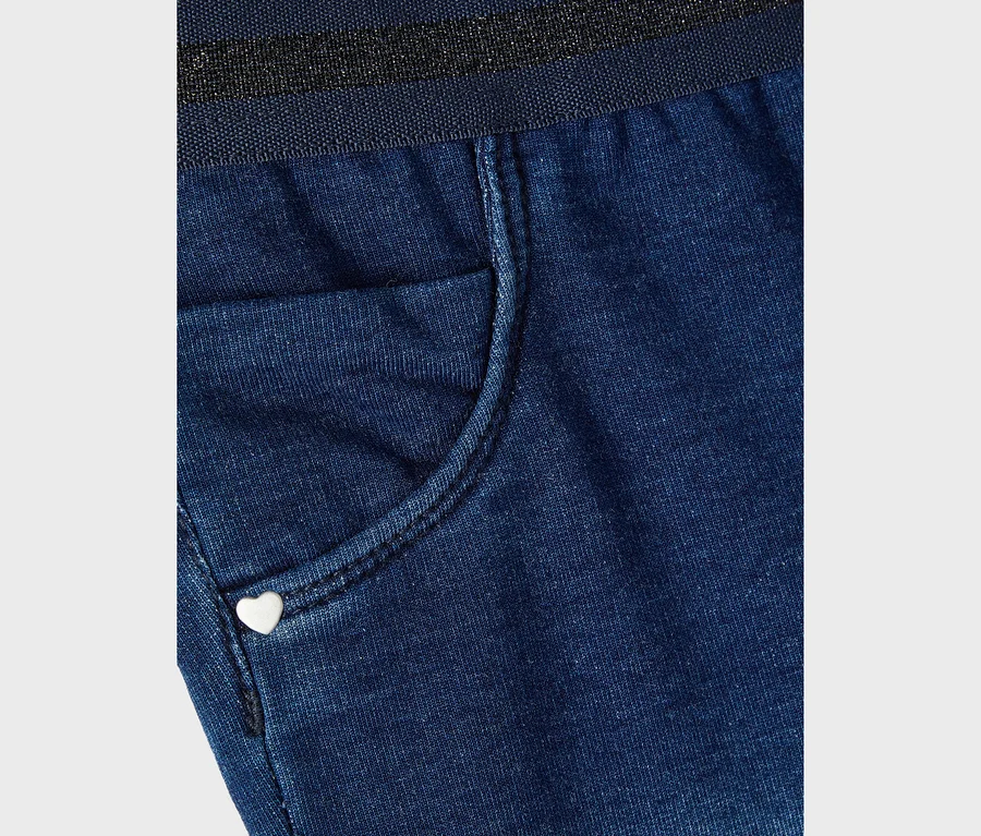 Gros plan sur un pantalon en jean bleu avec une petite poche et un bouton en forme de cœur.