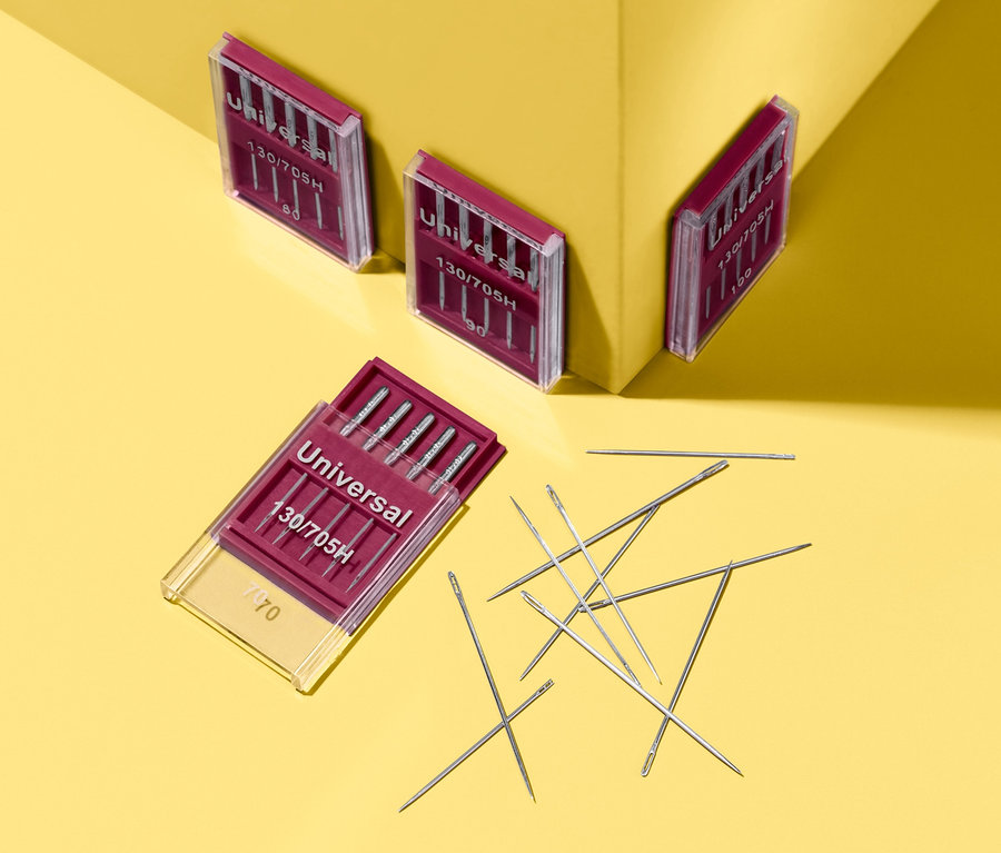 Sur un fond jaune, il y a quatre kits d'aiguilles pour coudre à la machine ou à la main.