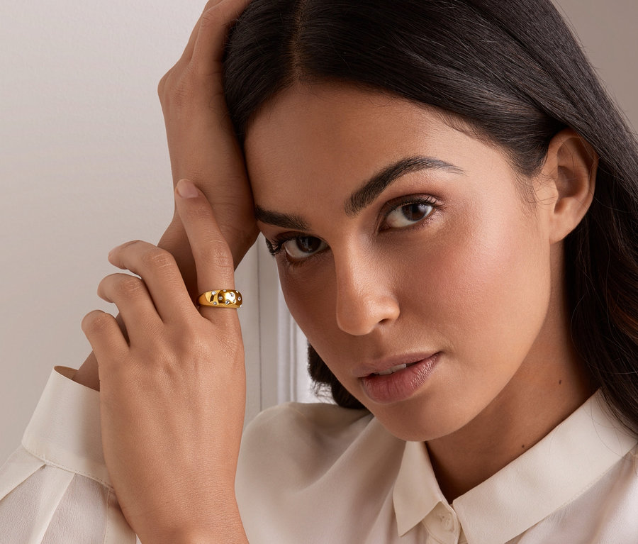 Une femme s'appuie sur sa main, un anneau doré avec des cristaux de verre à son doigt.