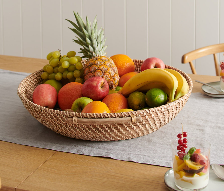 Une corbeille à fruits en rotin XXL remplie de divers fruits est posée sur une table.