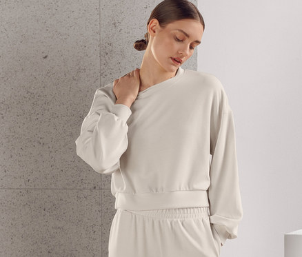 Une femme pose dans un survêtement beige très doux, composé d'un sweat-shirt et d'un pantalon.