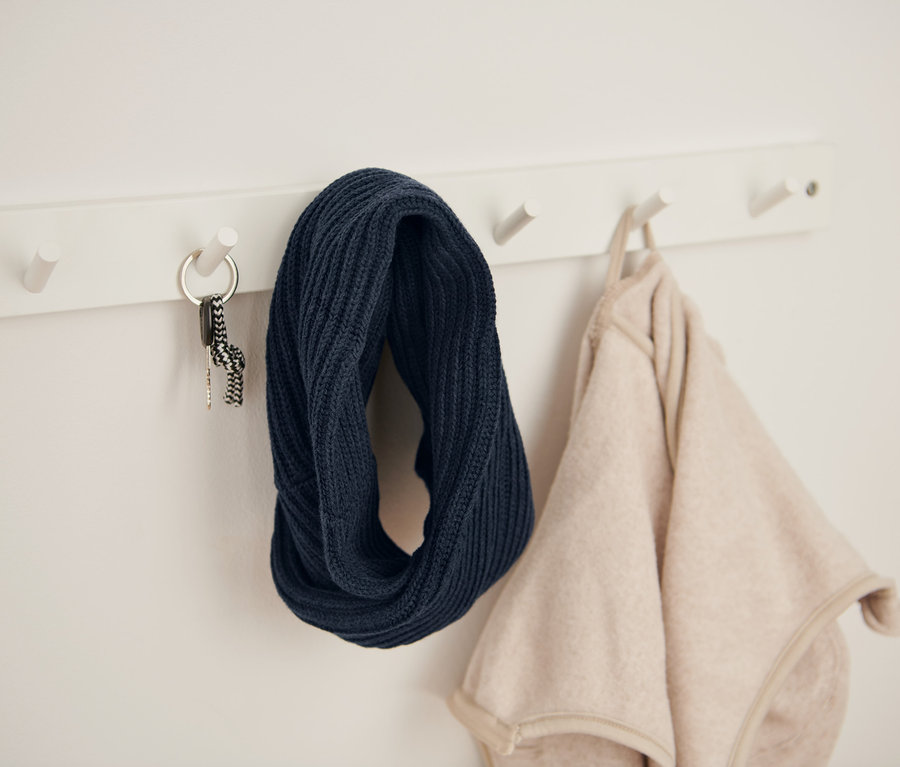 Un porte-manteau mural blanc avec une écharpe-tube en maille bleu marine, des clés et une veste beige.