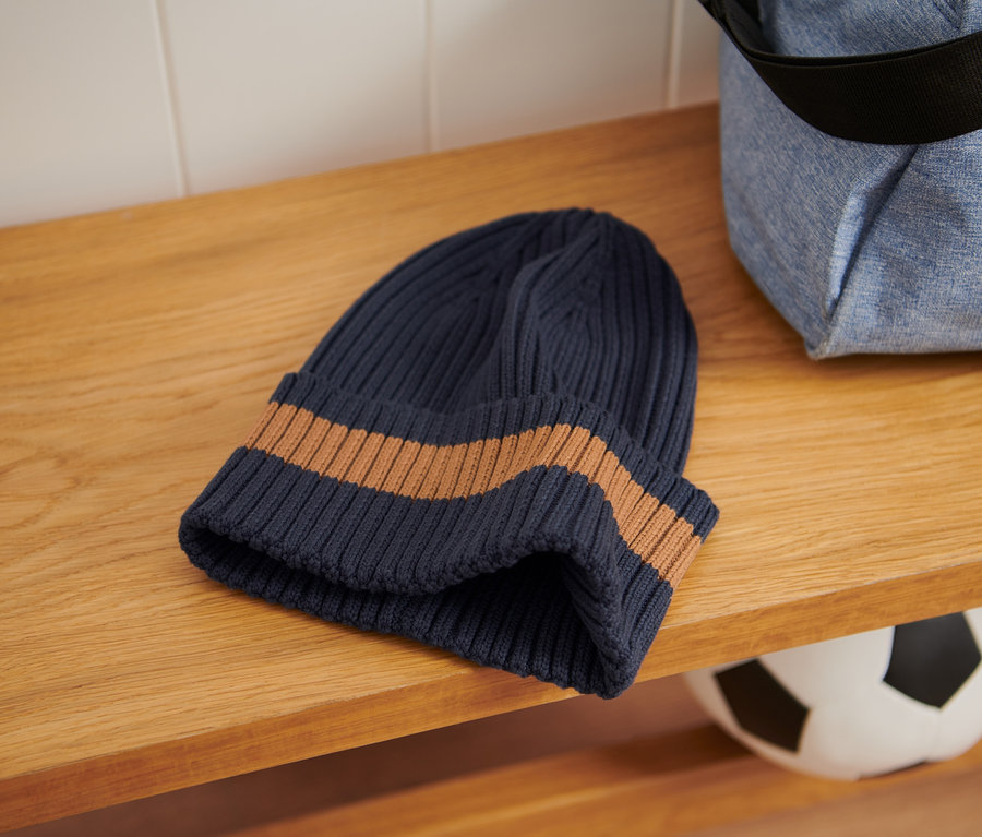 Un bonnet en maille et un sac de sport sont posés sur une étagère en bois.